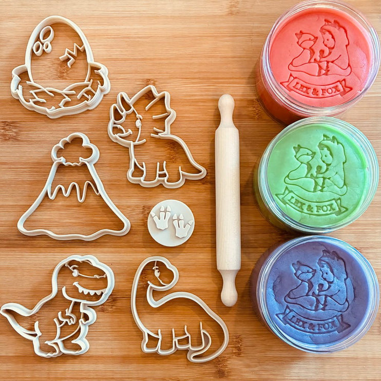 A set of dinosaur-themed cutters and a rolling pin with three playdough jars