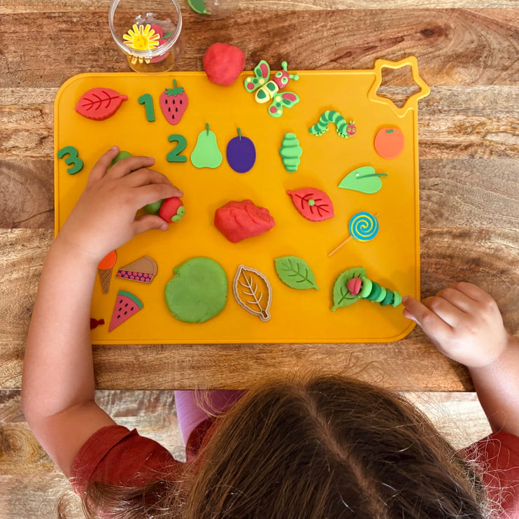 Child playing with colorful play dough shapes on a yellow mat with numbers and letters.
