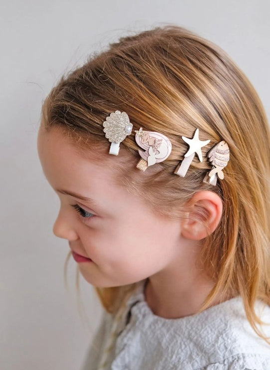 A young girl wearing a set of four decorative hair clips shaped like seashells, a starfish, and sea urchins