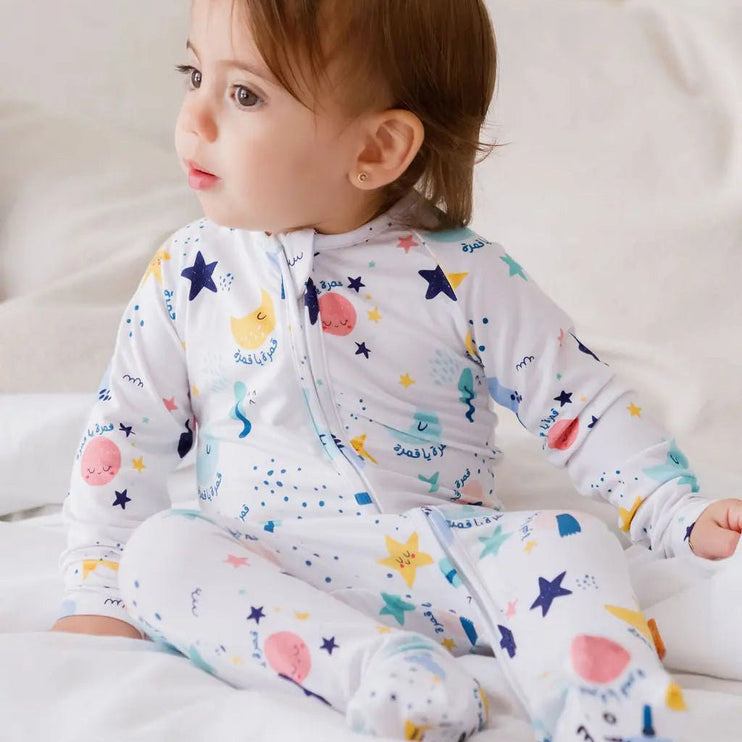 Baby wearing a colorful onesie with stars and moons on a white background
