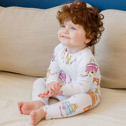 Child wearing a Bosta onesie with colorful bus patterns sitting on a beige couch.