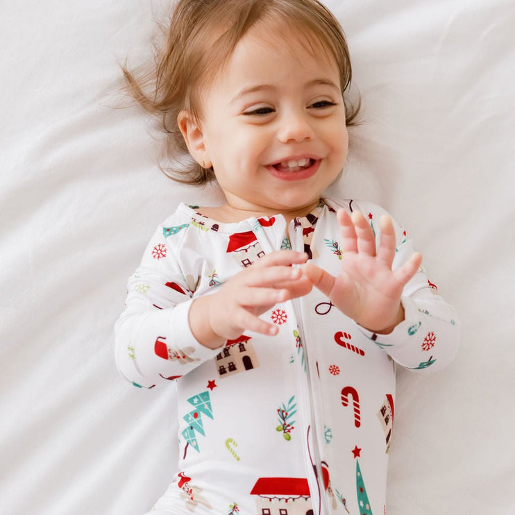 A baby wearing a Christmas-themed onesie with Santa Claus, reindeer, and holiday decorations.
