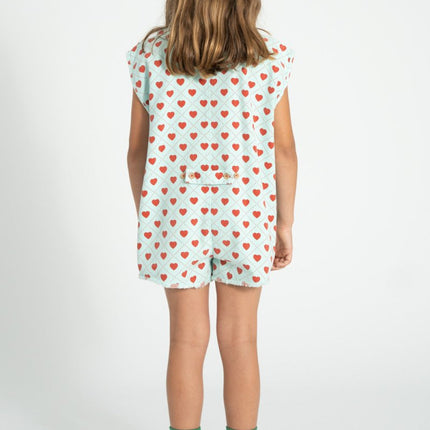 Child wearing a short sleeveless top with red heart pattern and shorts on a white background