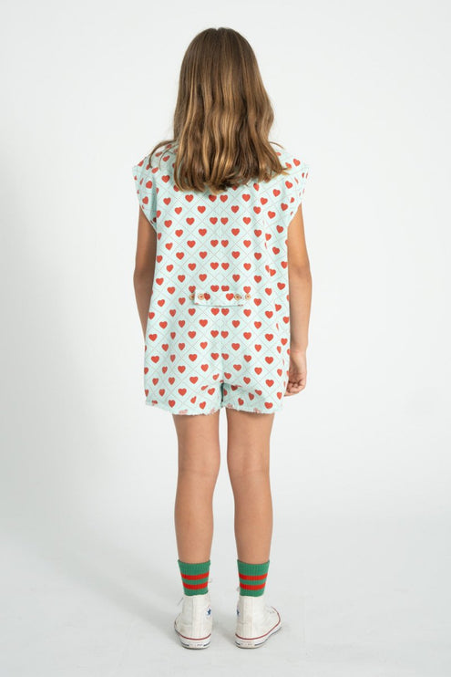 Child wearing a short sleeveless top with red heart pattern and shorts on a white background