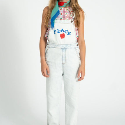 young girl wearing sleeveless top pairing a denim overall with 'peace' print