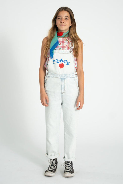 young girl wearing sleeveless top pairing a denim overall with 'peace' print