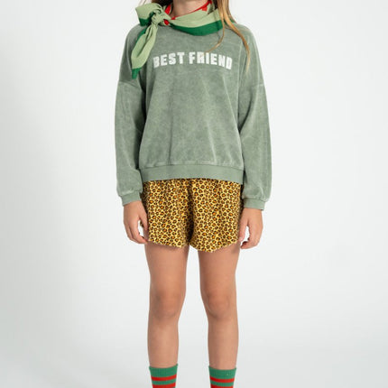 girl wearing a green 'BEST FRIENDS' sweatshirt, yellow patterned shorts, and green socks with a white background