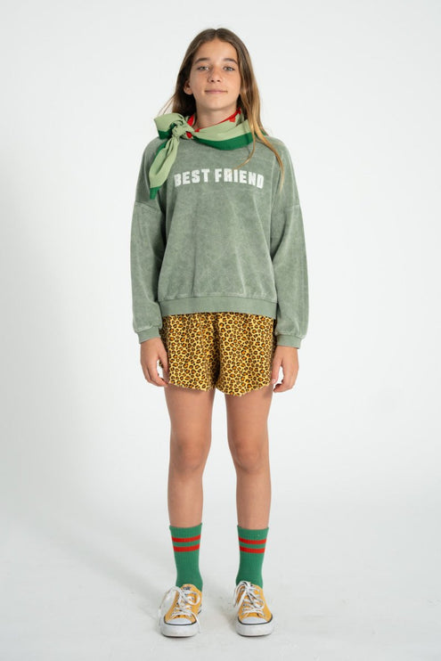 girl wearing a green 'BEST FRIENDS' sweatshirt, yellow patterned shorts, and green socks with a white background