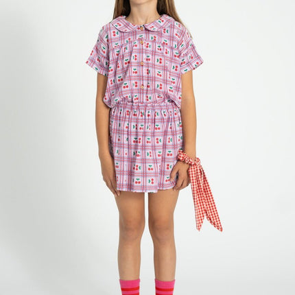 Kid wearing a lilac with cherries patterned outfit with a peter pan collar shirt  on a white background