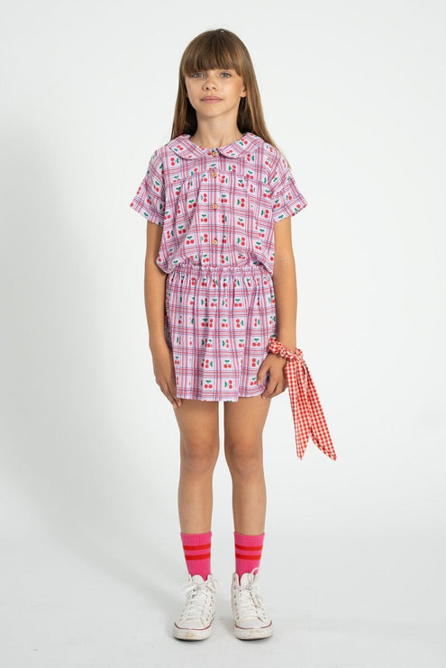 Kid wearing a lilac with cherries patterned outfit with a peter pan collar shirt  on a white background