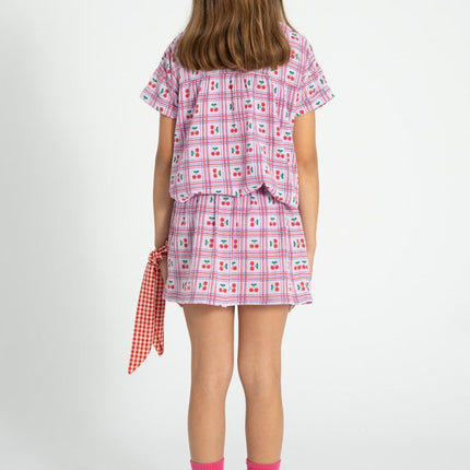 Kid wearing a lilac with cherries patterned outfit with a peter pan collar shirt  on a white background
