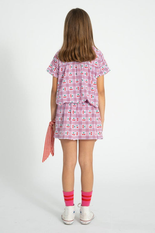 Kid wearing a lilac with cherries patterned outfit with a peter pan collar shirt  on a white background