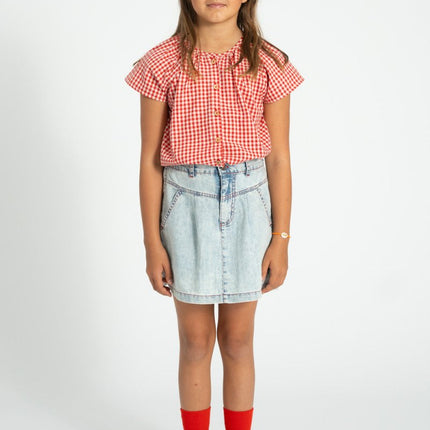 Young girl wearing a red and white checkered shirt, denim skirt, and red socks 