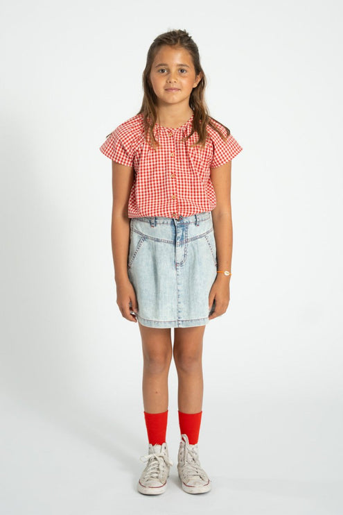 Young girl wearing a red and white checkered shirt, denim skirt, and red socks 