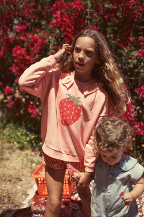 Girl wearing light pink sweatshirt  with collar and strawberry print
