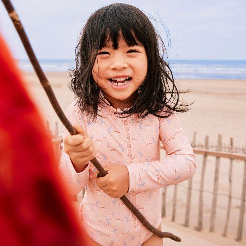 Cheerful baby girl wearing a colourful longsleeves swim suit with mimosa prints