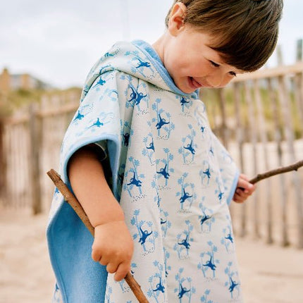 Boy wearing cream swim poncho with blue monkey print