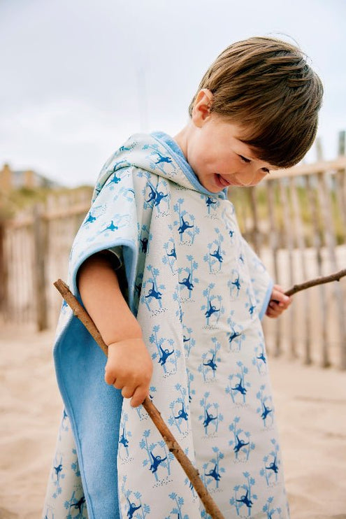 Boy wearing cream swim poncho with blue monkey print