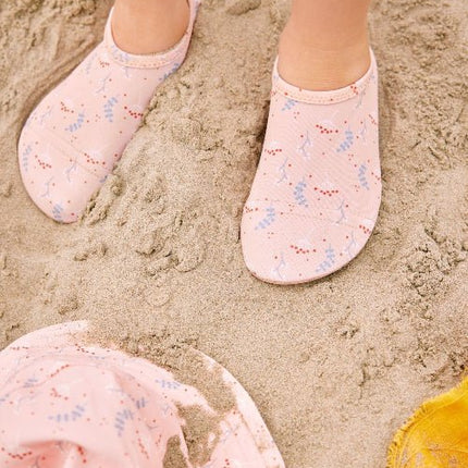 Baby wearing peach and mimosa print swim shoes and matching bucket hat on sandy beach