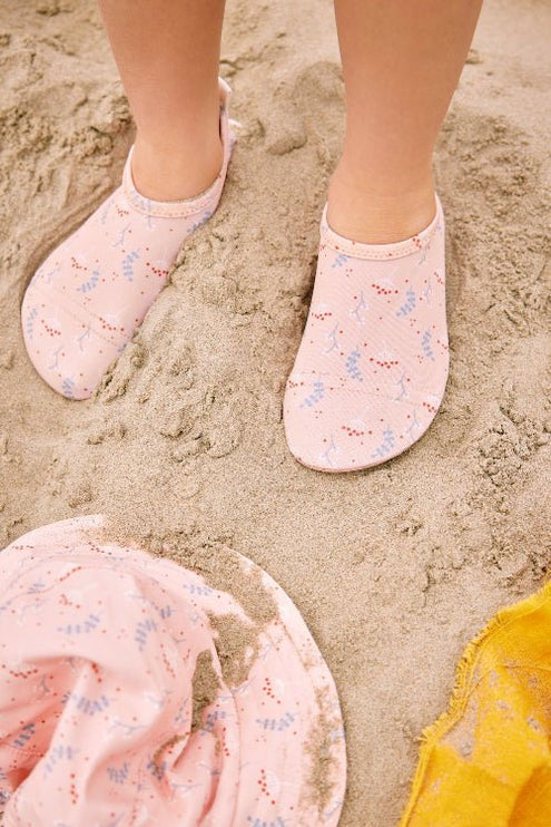 Baby wearing peach and mimosa print swim shoes and matching bucket hat on sandy beach
