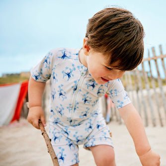 Cheerful baby boy wearing a cream swimsuit with blue monkey prints