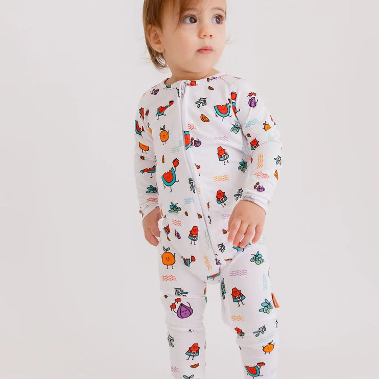 Child wearing a white onesie with colorful fruit patterns on a plain background