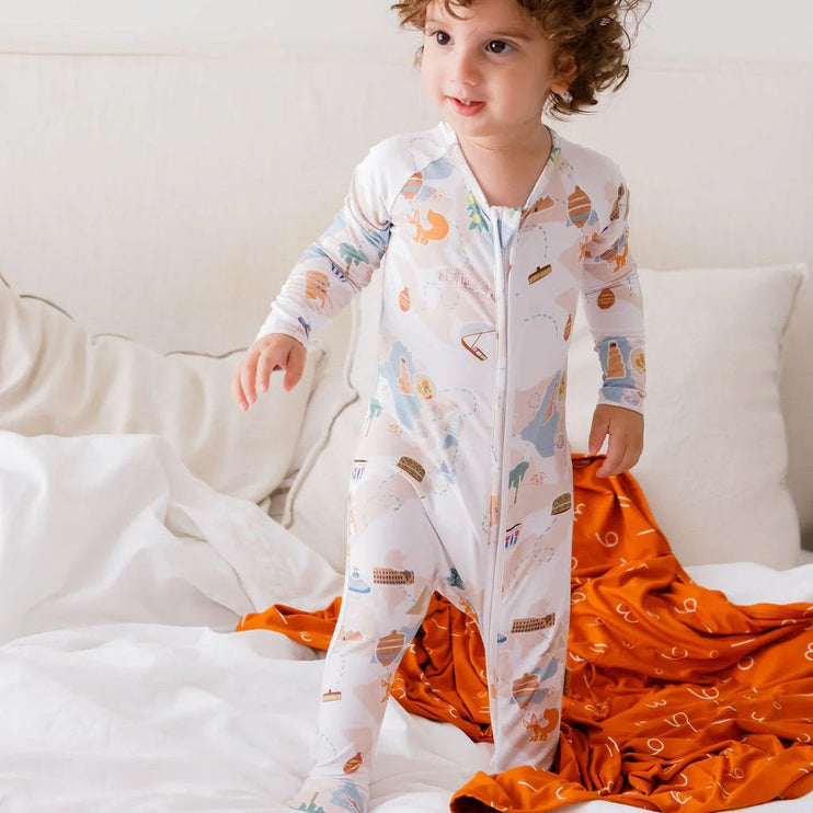 Child wearing a patterned onesie on a bed with an orange blanket