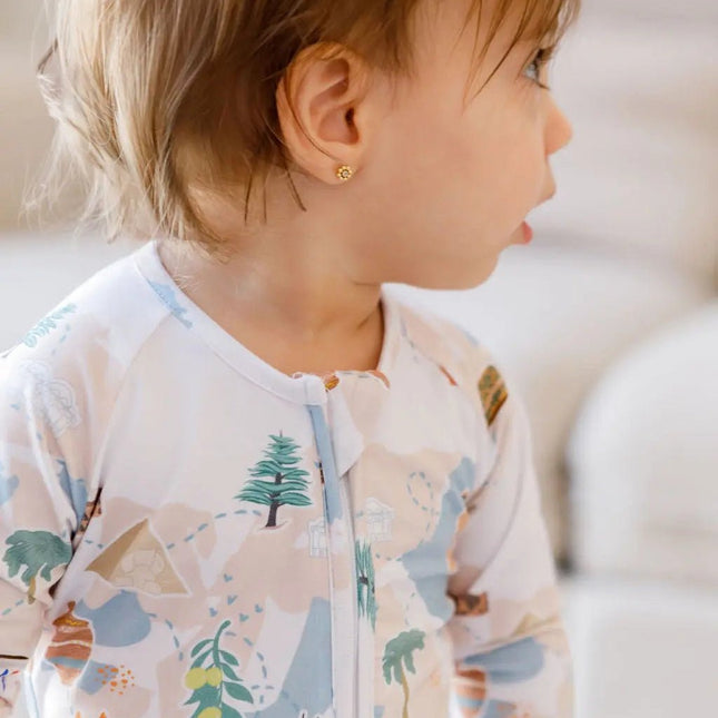 Child wearing a patterned onesie with trees and animals on a light background