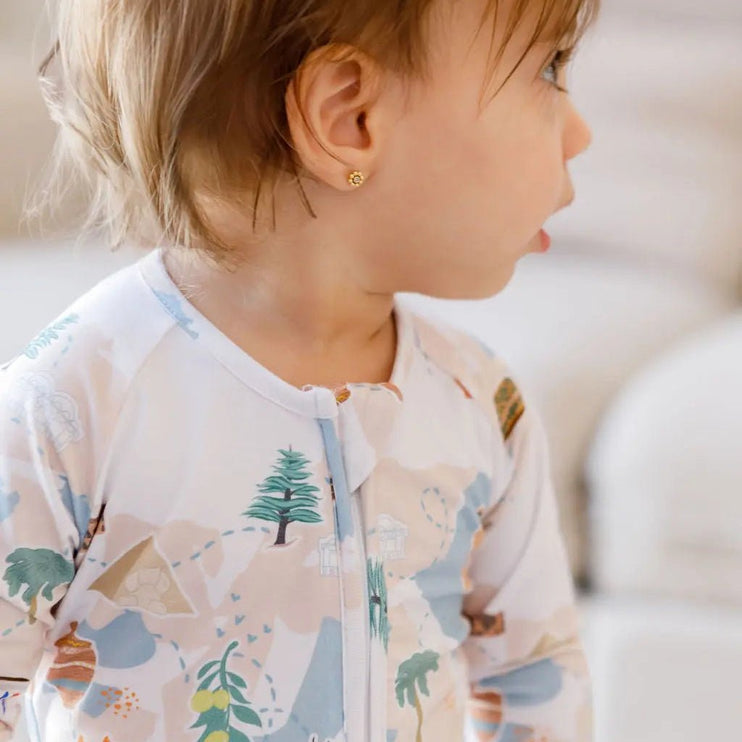 Child wearing a patterned onesie with trees and animals on a light background