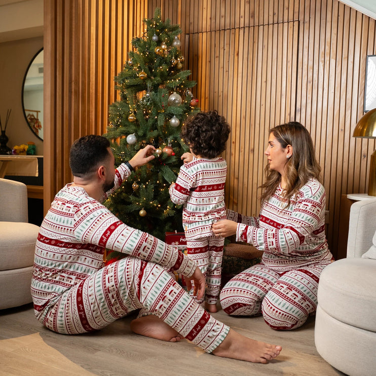 Family in matching christmss pajamas decorating a Christmas tree in a living room.