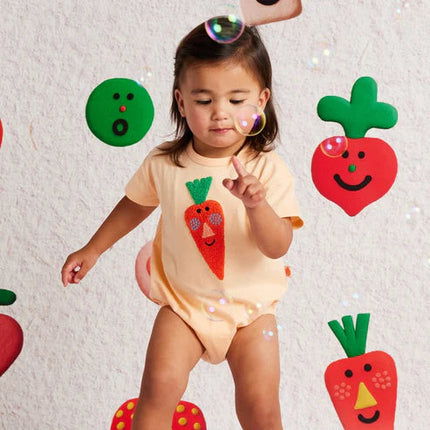 Child wearing a onesie with carrot design in a playful setting with cartoon vegetables.