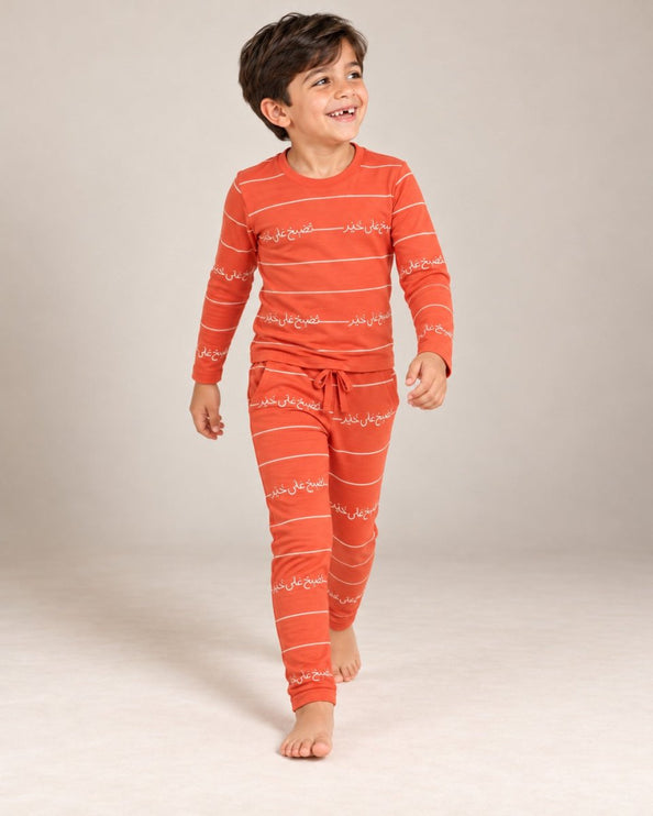 A young boywearing a matching two-piece orange pajama set with white horizontal stripes and Arabic calligraphy print