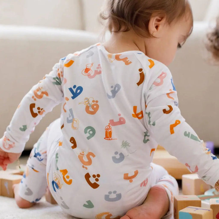 Baby wearing a onesie with colorful letters and shapes.