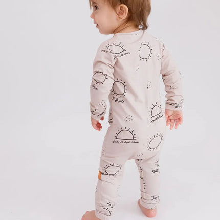 Baby wearing a light-colored onesie with sun designs on a white background