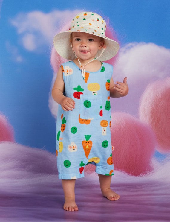 Child wearing a colorful outfit with veggie print patterns and a hat